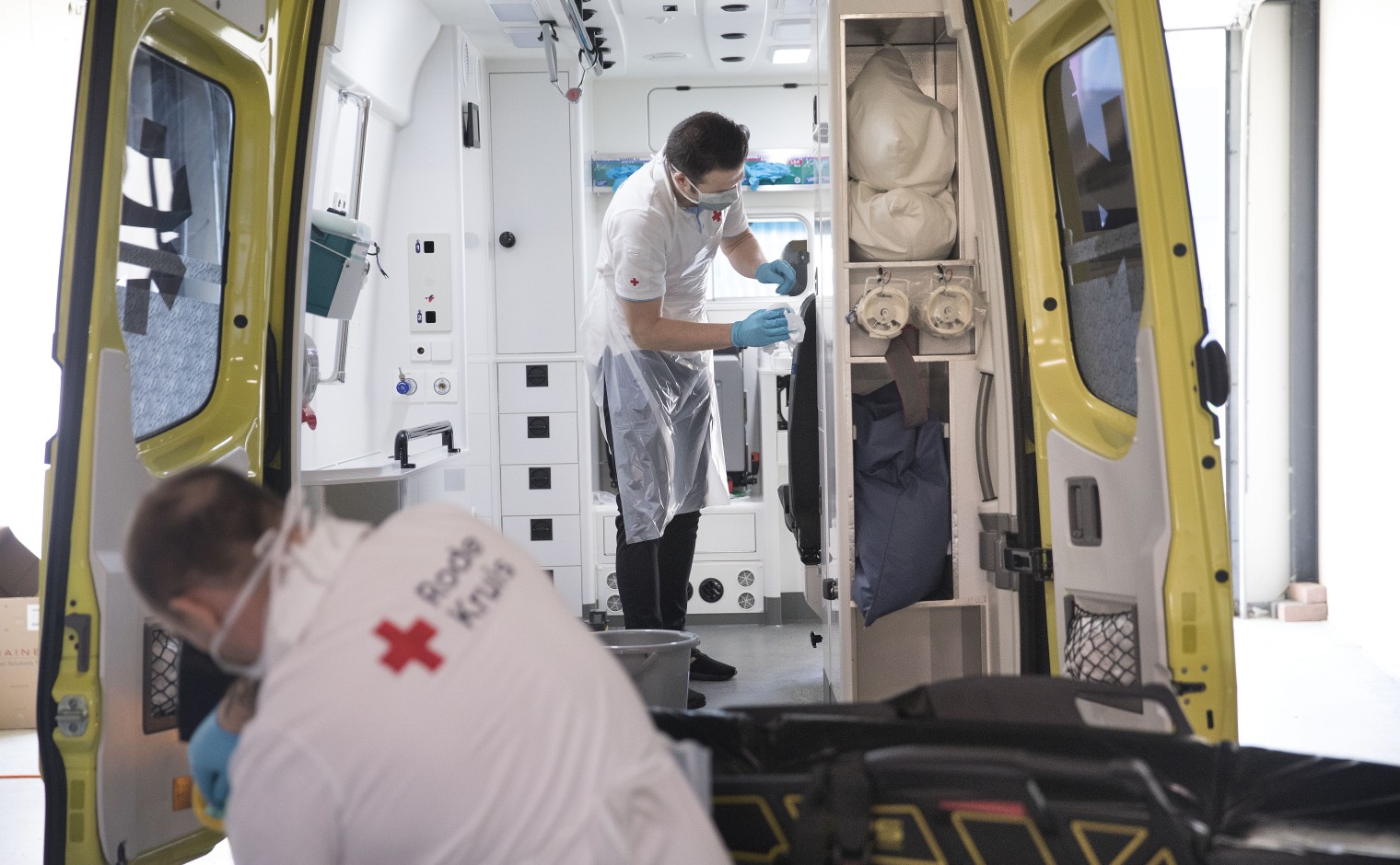 Medewerkers van hr Rode Kruis ontsmetten een ambulance tijdens de Coronacrisis.