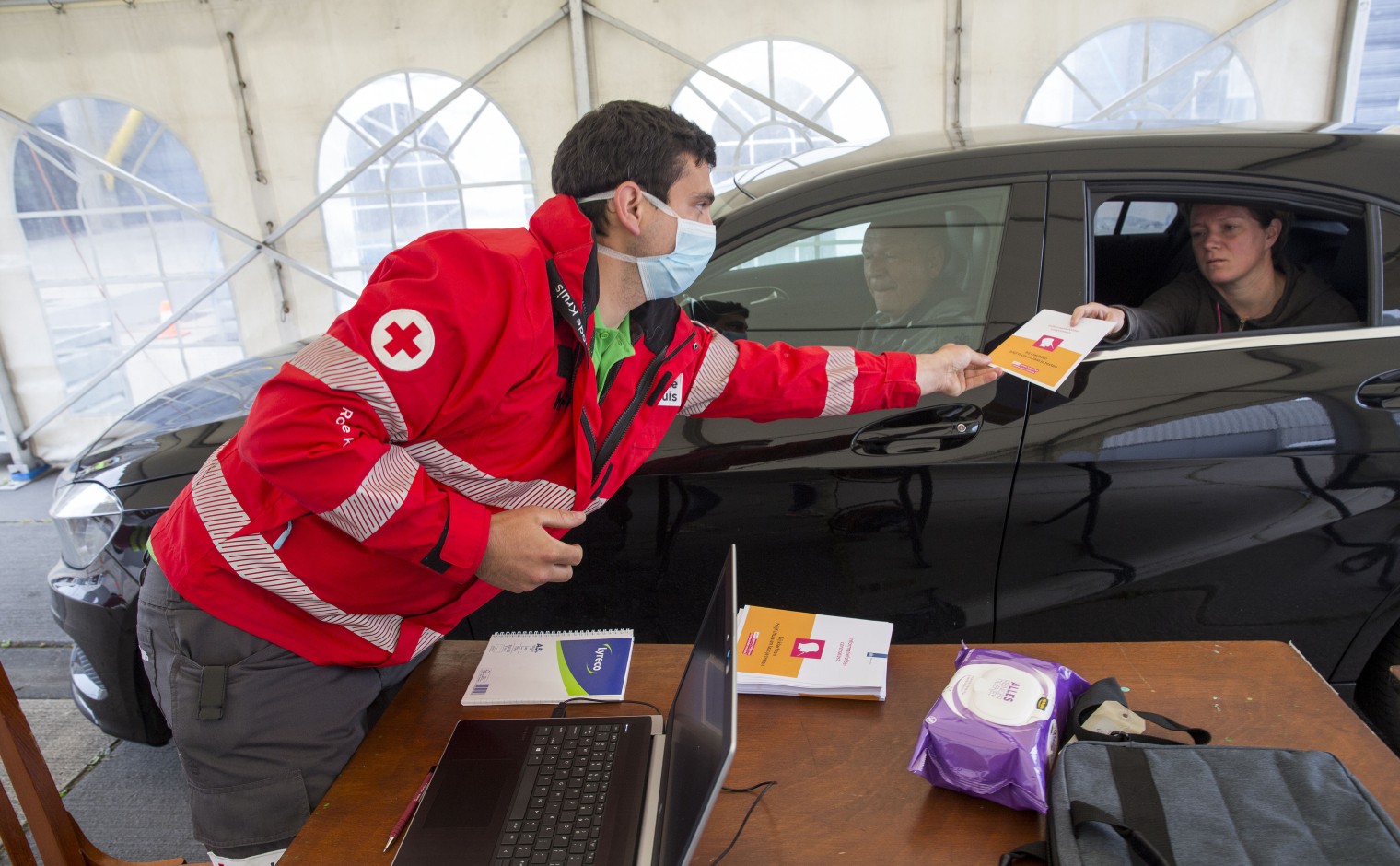 Een vrijwilliger van het Rode Kruis reikt een boekje uit in een coronateststraat.